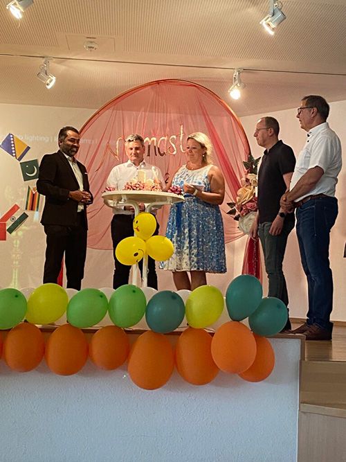 Teilnehmer*innen des Festes haben sich auf einer kleinen Bühne um einen Kuchen mit leuchtenden Kerzen versammelt.