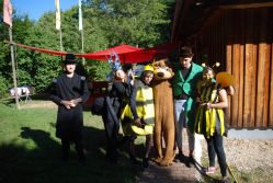 Mehrere Betreuerinnen und Betreuer in fantasievollen Kostümen posieren lachend vor einer Holzhütte.