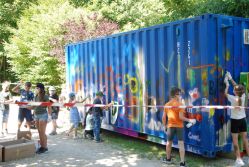 Kinder besprühen kreativ einen blauen Container mit bunter Farbe bei einer Graffiti-Aktion.