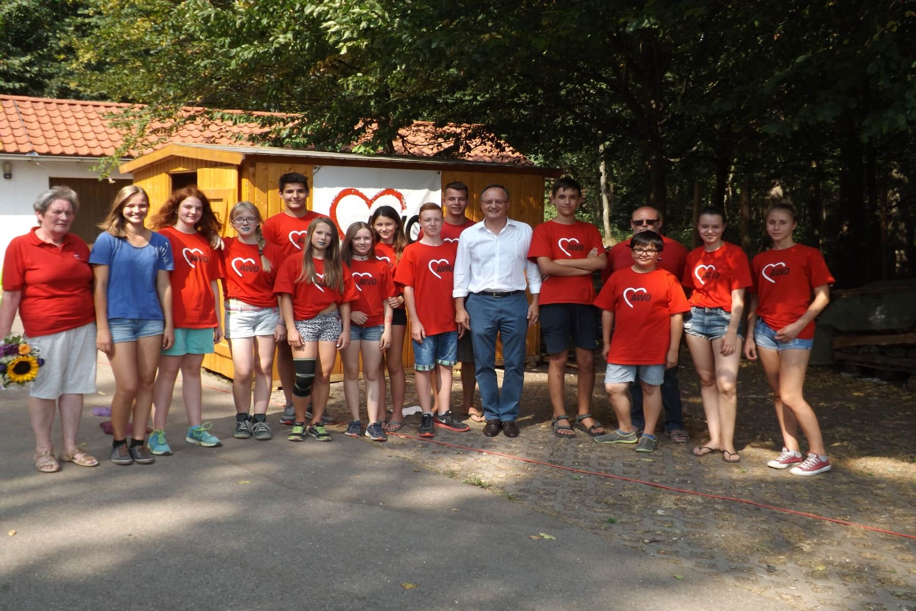 Gruppenfoto von Jugendlichen und Erwachsenen in AWO-Shirts vor einer Holzhütte.