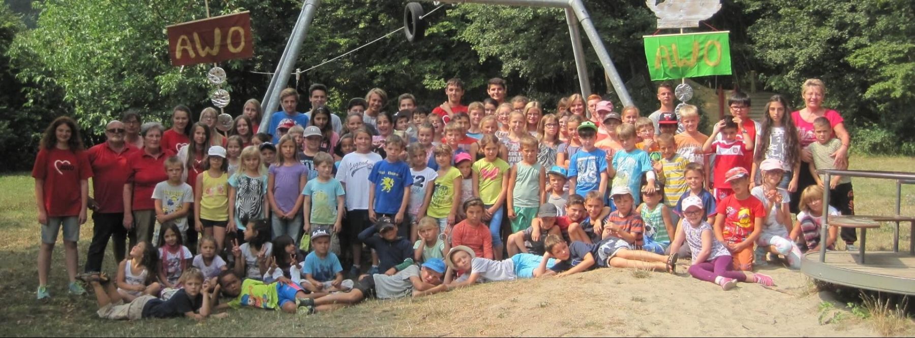 Großes Gruppenfoto mit vielen Kindern und Betreuern unter AWO-Schildern im Freien.